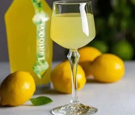 Bottle of homemade Limoncello with fresh lemons and herbs on a wooden table.