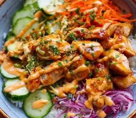 Bowl of Spicy Bang Bang Chicken topped with fresh vegetables and sauce